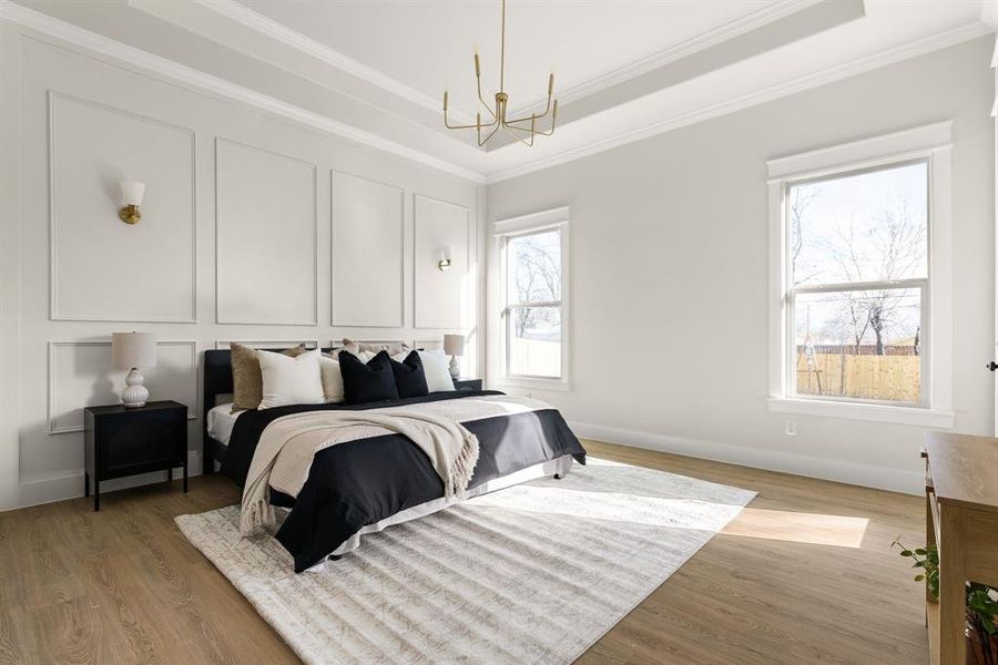 Bedroom featuring a notable chandelier, a tray ceiling, ornamental molding, and light wood-style floors