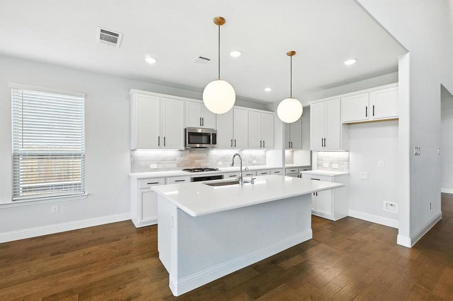 Stylish and sleek kitchen with modern lighting, wood floors, white cabinets and light countertops with gas cooktop and SS appliances.
