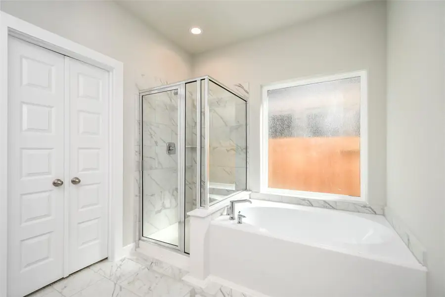 Escape to a spa-like oasis in this primary bathroom. Enjoy a walk-in shower with tile surround, a separate garden tub with custom detailing, and an elegant vanity featuring light countertops, modern hardware, and beautiful recessed lighting. Experience luxury and relaxation in every detail. Sample photo of completed home with similar floor plan. Actual colors and selections may vary.