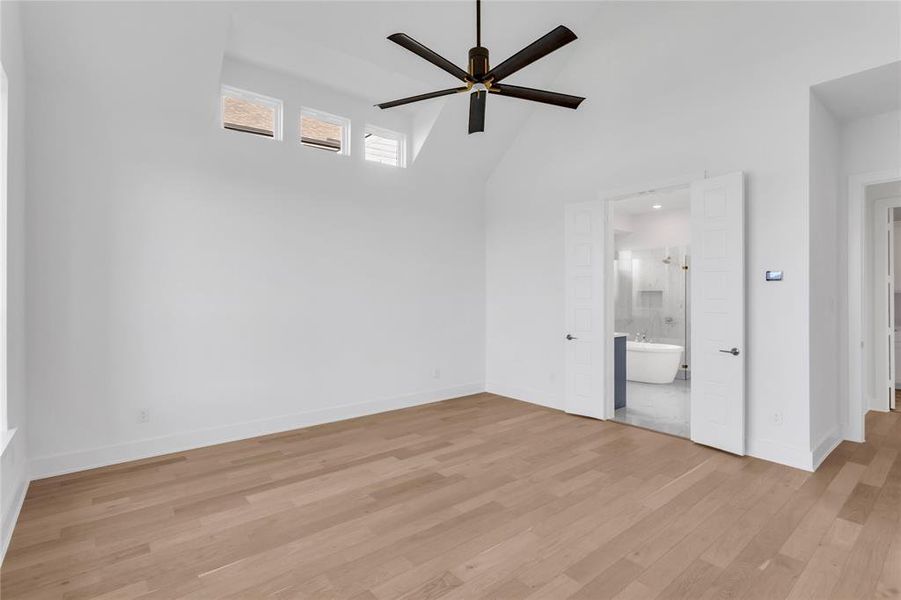 Unfurnished bedroom featuring light wood-type flooring, high vaulted ceiling, a ceiling fan, and ensuite bath