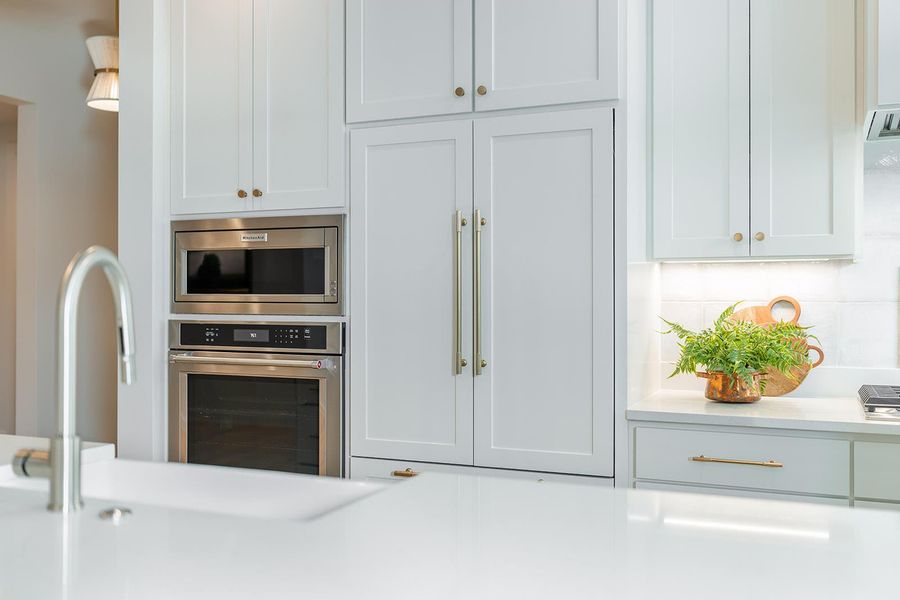 Kitchen featuring built in appliances, white cabinets, backsplash, and light stone countertops