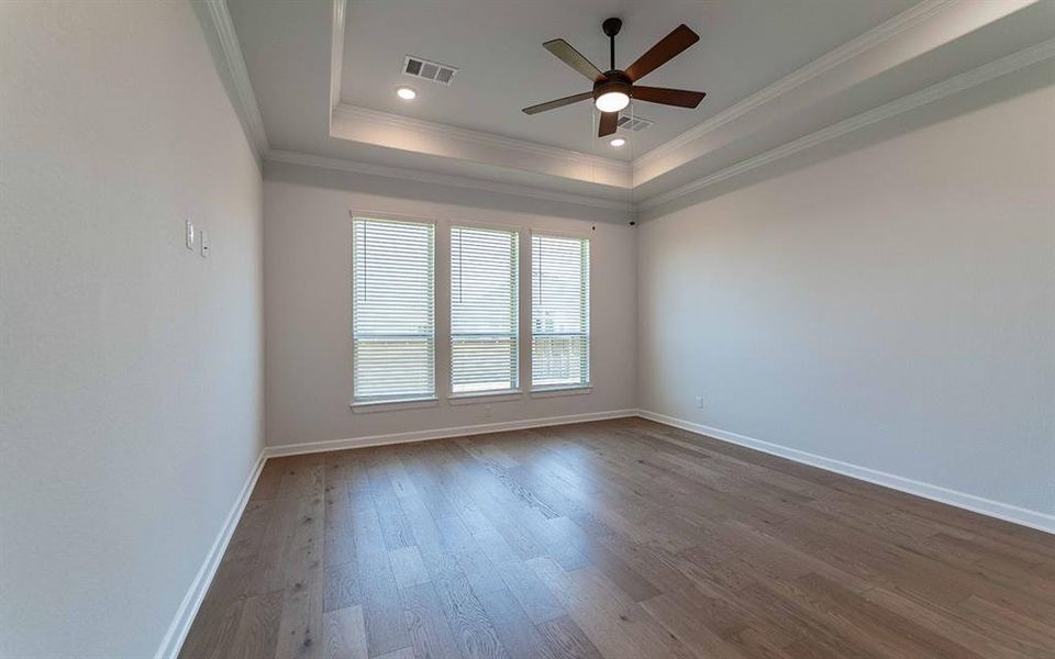 Spacious room featuring wood-finish flooring, a tiered tray ceiling with recessed lighting, and a ceiling fan Spacious room featuring wood-finish flooring, a tiered tray ceiling with recessed lighting, and a ceiling fan
