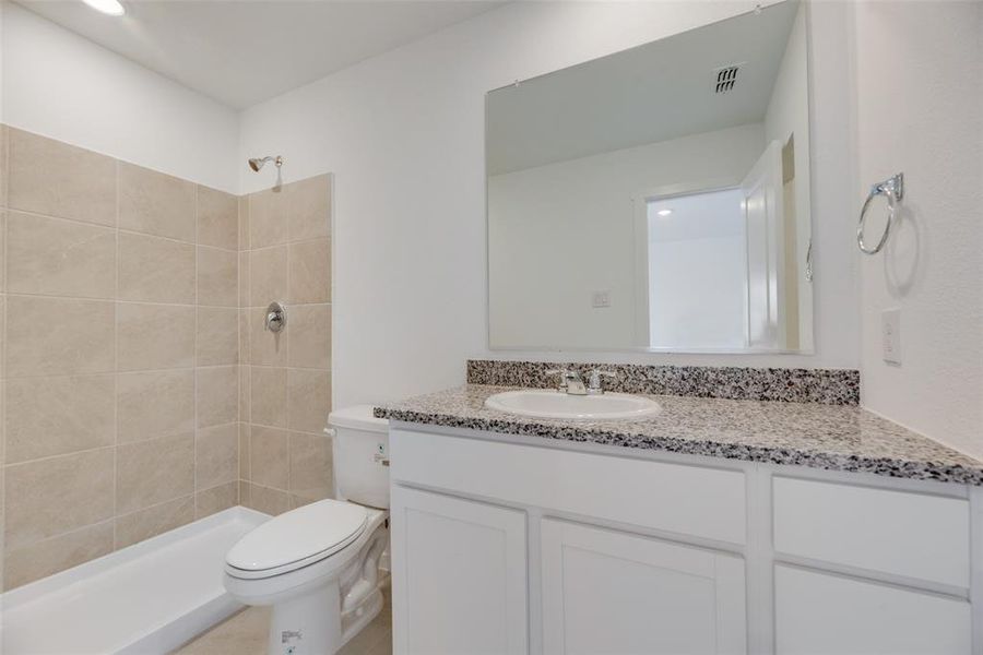 Bathroom with vanity, a tile shower, and toilet