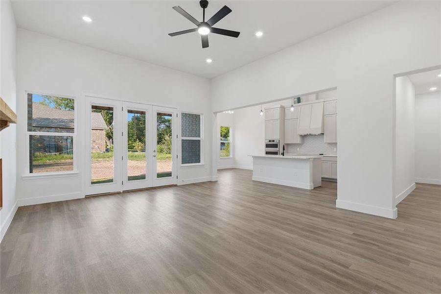 Spacious open-concept living area featuring wood-finish flooring, high ceilings with recessed lighting, and a contemporary ceiling fan