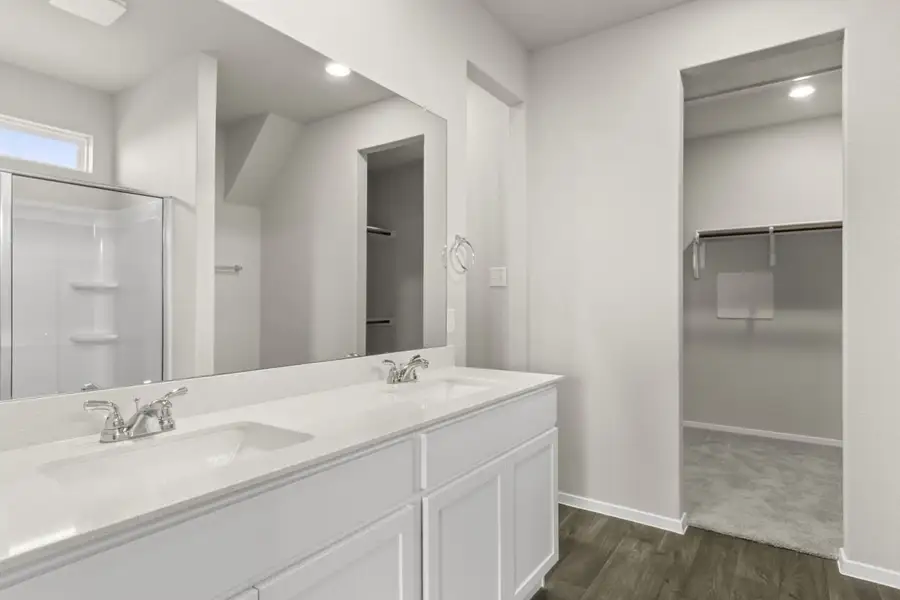 Image of primary bathroom with white cabinets and vanity with a mirror and a connected walk in closet