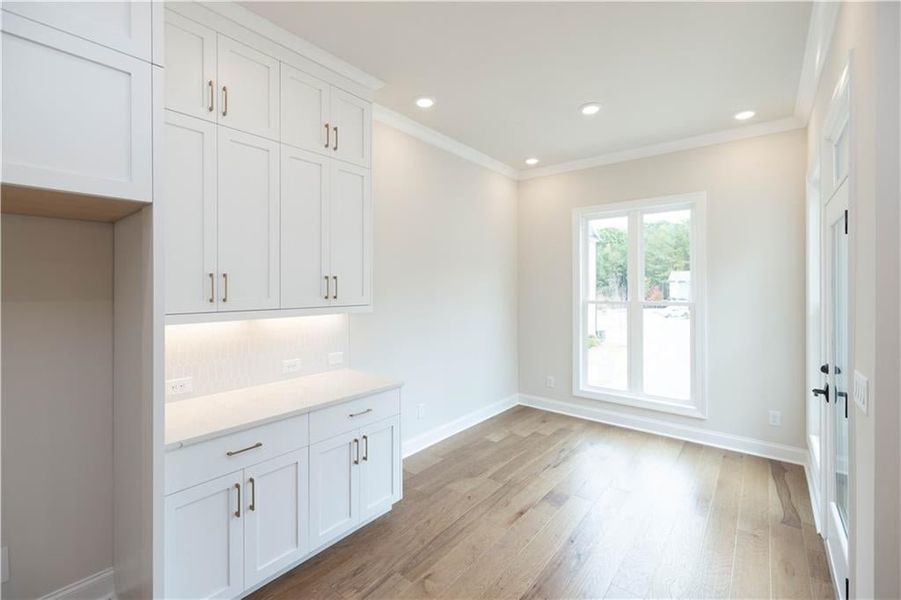 Kitchen featuring white cabinetry, ornamental molding, backsplash, and light hardwood / wood-style floors