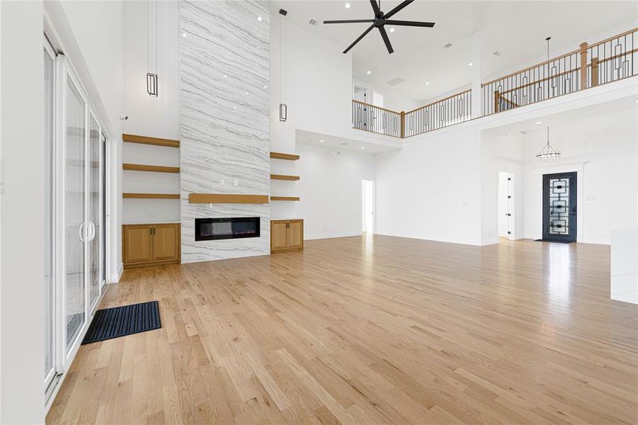 Unfurnished living room featuring a high ceiling, a premium fireplace, a ceiling fan, and light wood-style flooring Unfurnished living room featuring a high ceiling, a premium fireplace, a ceiling fan, and light wood-style flooring