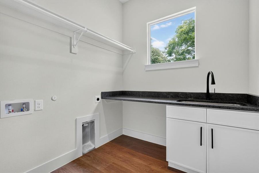 Dedicated utility space featuring wood-finish flooring, a built-in sink with a matte black faucet, and white cabinetry