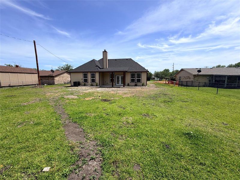 Expansive backyard with a large patio featuring a covered area, two exterior doors, and a central chimney