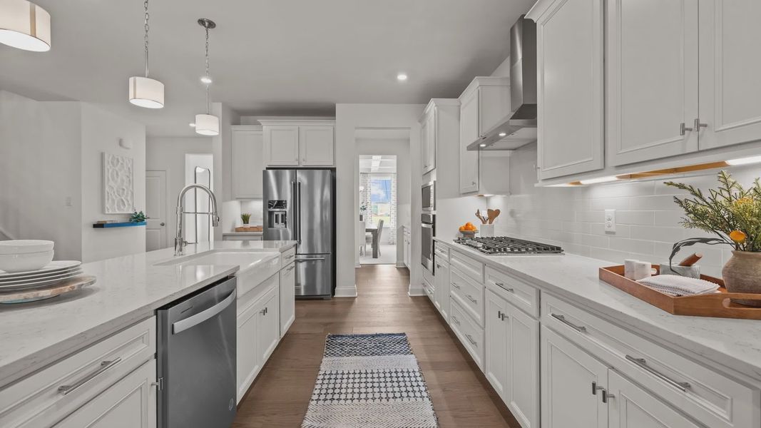 Gourmet kitchen with white farmhouse sink, gas cooktop, vented hood, and premium lighting; the Townsend Design by DRB Homes
