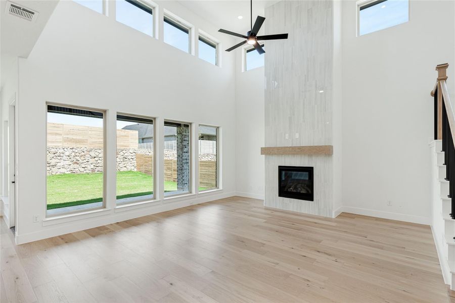 Open living room with two-story ceilings, tile fireplace, hardwood floors, and large windows overlooking backyard