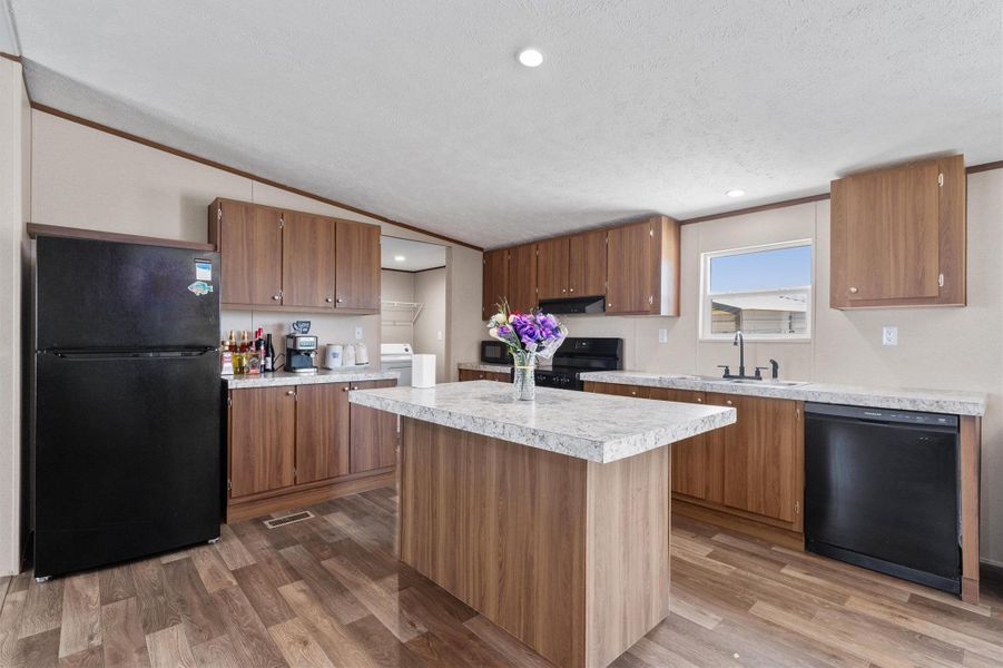 A spacious central island highlights this kitchen complete with warm wood cabinetry and durable vinyl flooring.