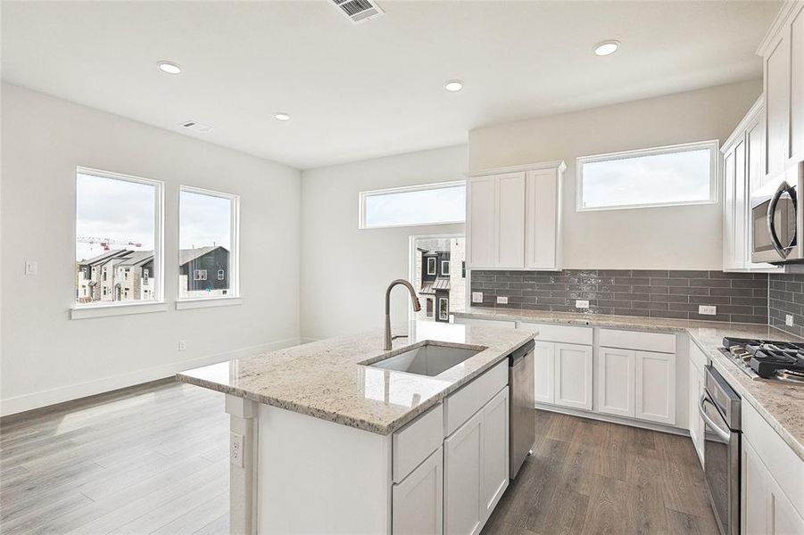 Kitchen with white cabinetry, tasteful backsplash, an island with sink, hardwood / wood-style floors, and sink