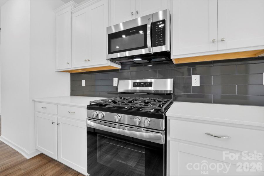 Clean, elegant white cabinets and 5-burner gas range with vented microwave