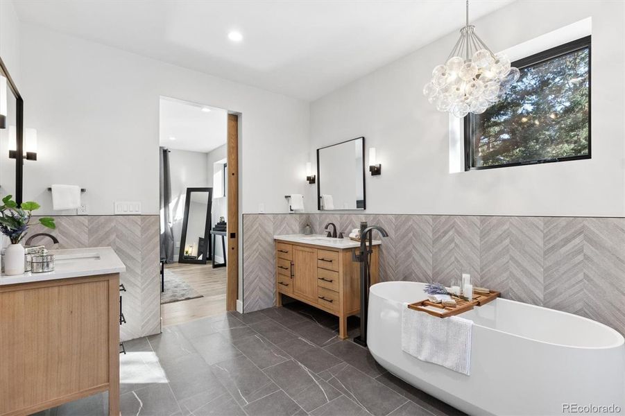 En-suite primary bathroom features designer lighting, gorgeous custom tile and solid wood vanities with stone countertops En-suite primary bathroom features designer lighting, gorgeous custom tile and solid wood vanities with stone countertops