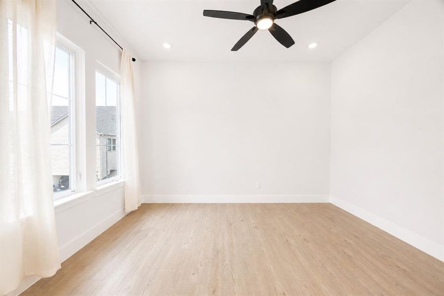 Bright room featuring light wood-finish flooring, white walls, and a black ceiling fan with integrated lighting