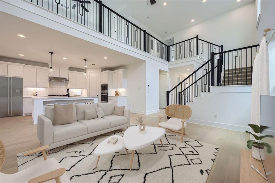 Virtually staged photo - Living area featuring a high ceiling, recessed lighting, light wood-type flooring, and stairway Virtually staged photo - Living area featuring a high ceiling, recessed lighting, light wood-type flooring, and stairway