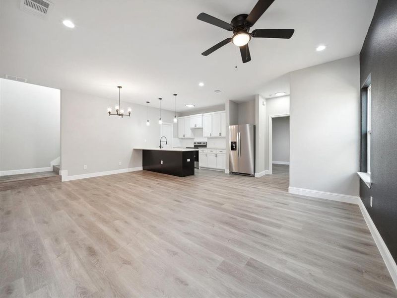 Unfurnished living room with ceiling fan with notable chandelier, sink, and light hardwood / wood-style flooring