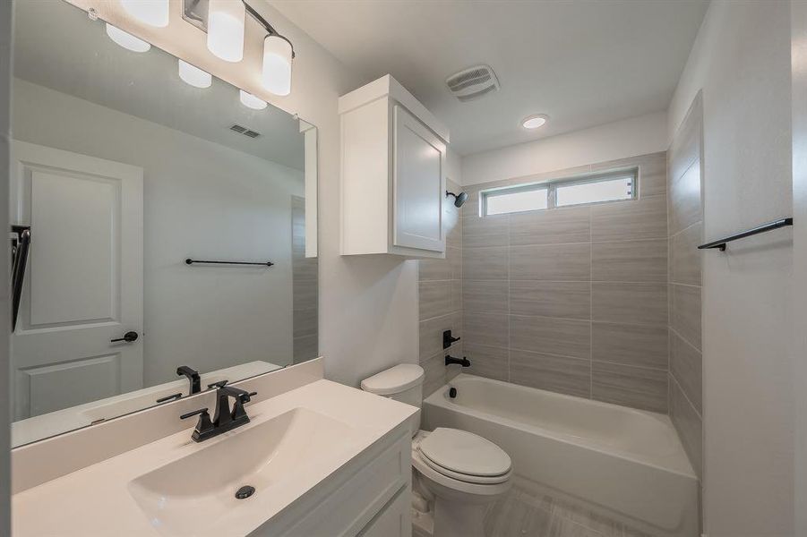 Bathroom featuring a vanity with an integrated sink, a large mirror, a tiled shower with a bathtub, and an overhead window