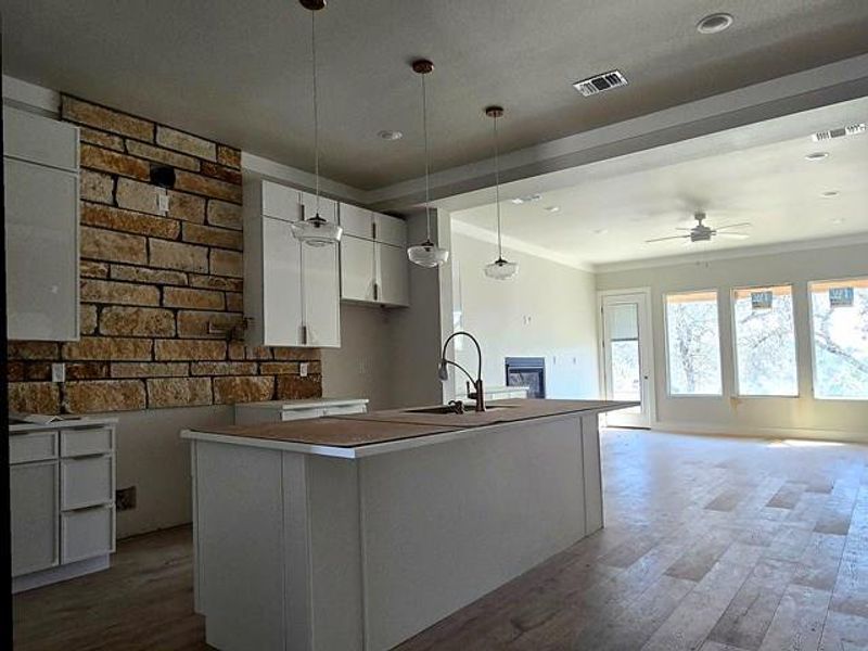 Kitchen featuring decorative light fixtures, an island with sink, a glass covered fireplace, light wood finished floors, and white cabinets