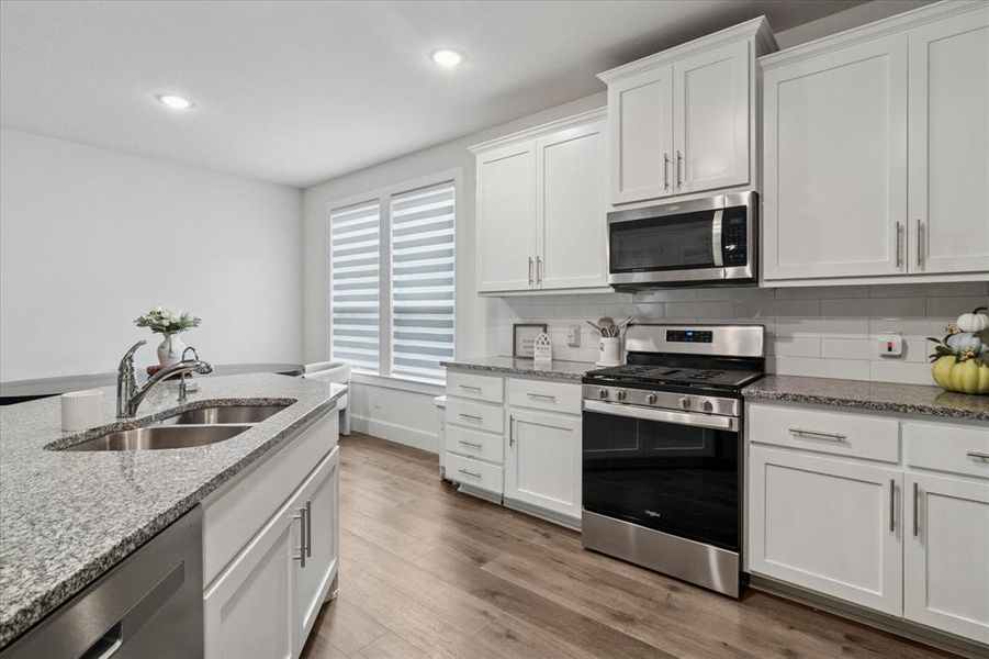 Kitchen featuring stainless steel appliances, white cabinetry, light stone counters, light wood-style floors, and tasteful backsplash Kitchen featuring stainless steel appliances, white cabinetry, light stone counters, light wood-style floors, and tasteful backsplash