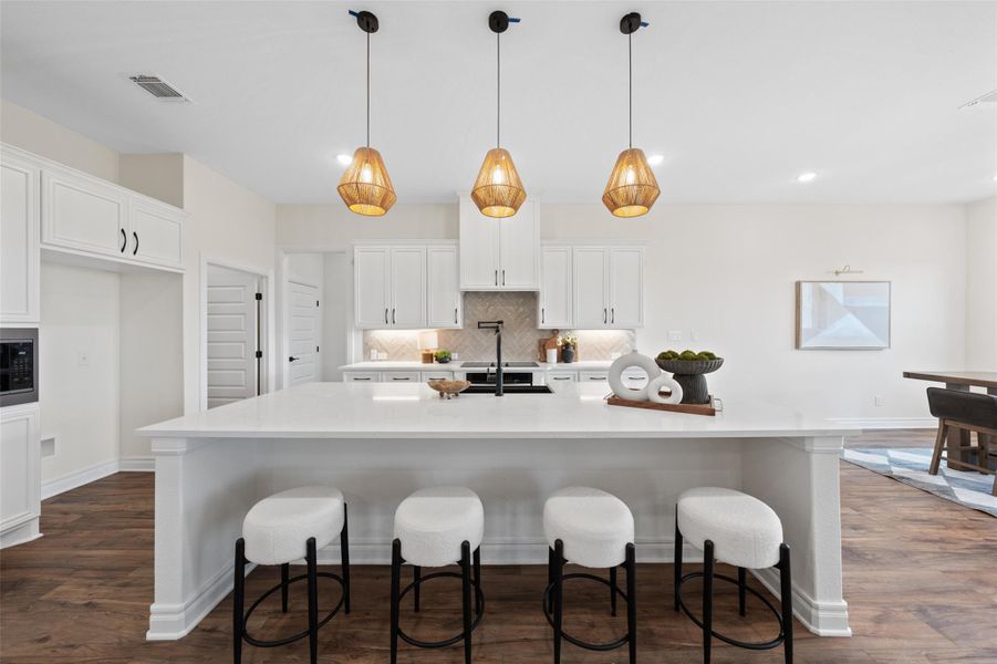 Kitchen with white cabinets, decorative backsplash, a breakfast bar area, hanging light fixtures, and a spacious island Kitchen with white cabinets, decorative backsplash, a breakfast bar area, hanging light fixtures, and a spacious island
