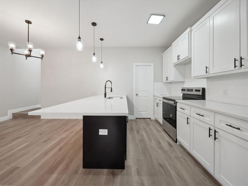 Kitchen with sink, a center island with sink, white cabinetry, hanging light fixtures, and stainless steel range with electric cooktop