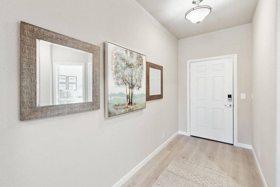 Narrow entryway with light wood floors, two framed mirrors, wall art, and a white six-panel front door Narrow entryway with light wood floors, two framed mirrors, wall art, and a white six-panel front door