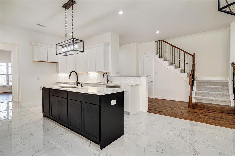 Kitchen with tasteful backsplash, a kitchen island with sink, sink, white cabinetry, and hanging light fixtures