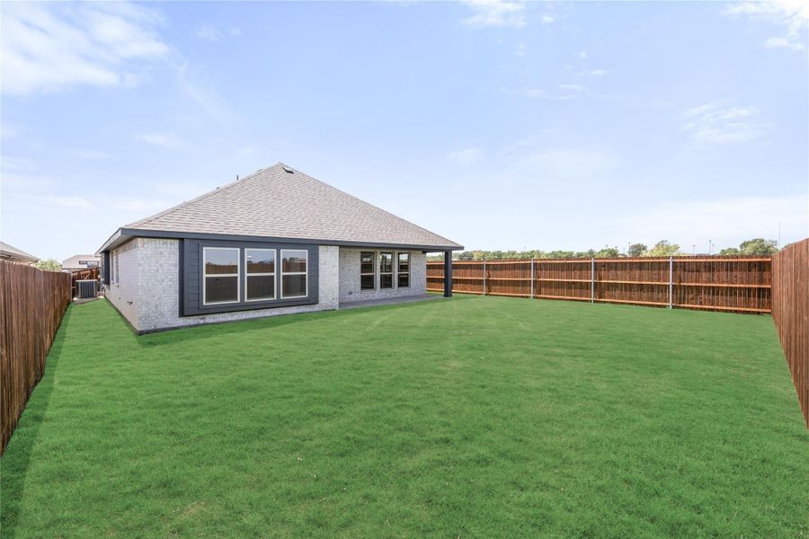 Backyard of single-story brick home with large green lawn and wood privacy fence on both sides.