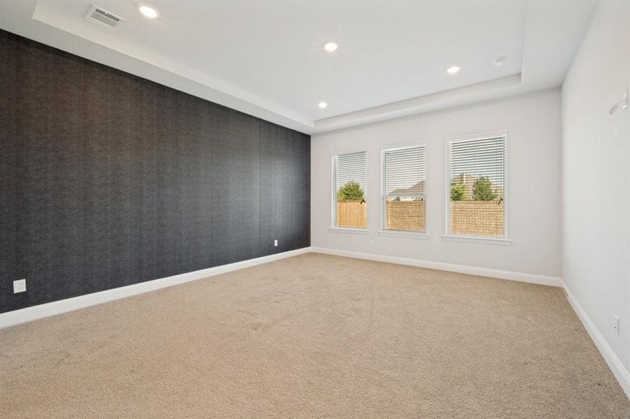 Spacious room with a dark textured accent wall, three windows with blinds, recessed lighting, and a tray ceiling