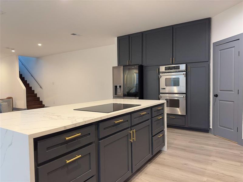 Kitchen featuring light hardwood / wood-style flooring, stainless steel appliances, gray cabinetry, light stone counters, and a kitchen island