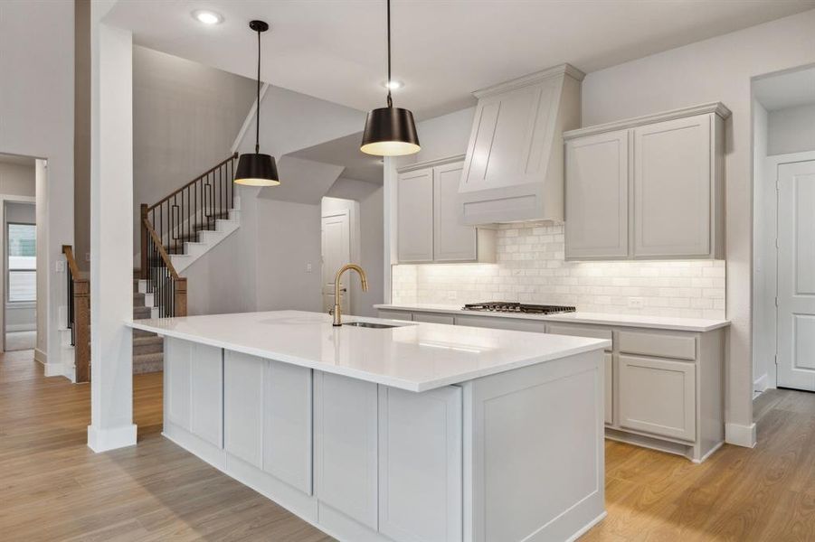 Kitchen with light wood-style flooring, backsplash, custom range hood, an island with sink, and recessed lighting