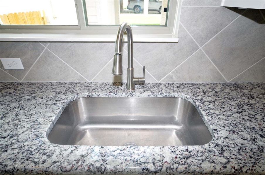 Stainless Undercounted kitchen sink is located under a kitchen window.