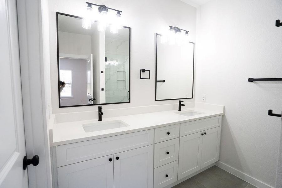 Bathroom with a marble finish shower, double vanity, and dark tile patterned flooring