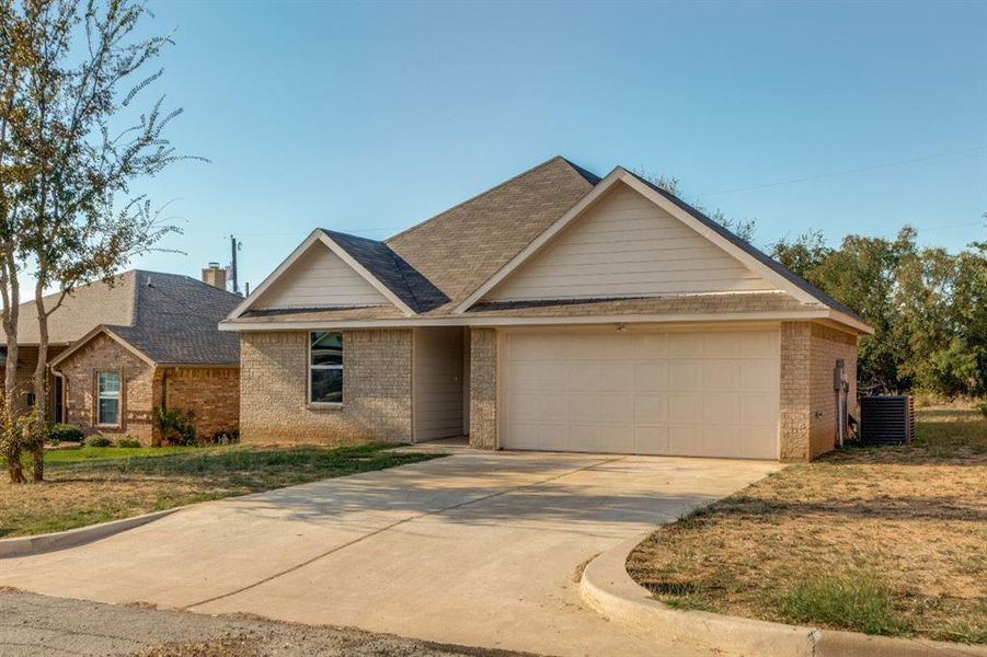 View of front of home featuring brick siding, a shingled roof, driveway, and an attached garage