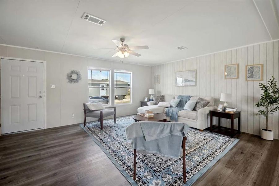 Living room with ceiling fan, crown molding, dark wood-type flooring, and wooden walls