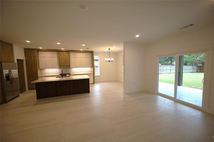 Kitchen featuring modern cabinets, stainless steel fridge with ice dispenser, backsplash, a center island with sink, and recessed lighting