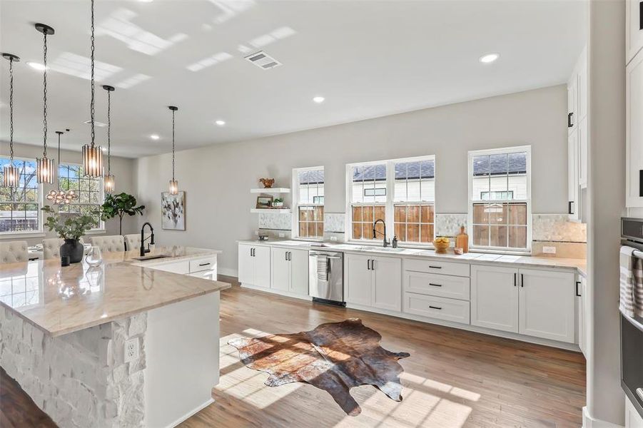 Kitchen featuring white cabinetry, light stone countertops, a large island, decorative light fixtures, and appliances with stainless steel finishes Kitchen featuring white cabinetry, light stone countertops, a large island, decorative light fixtures, and appliances with stainless steel finishes