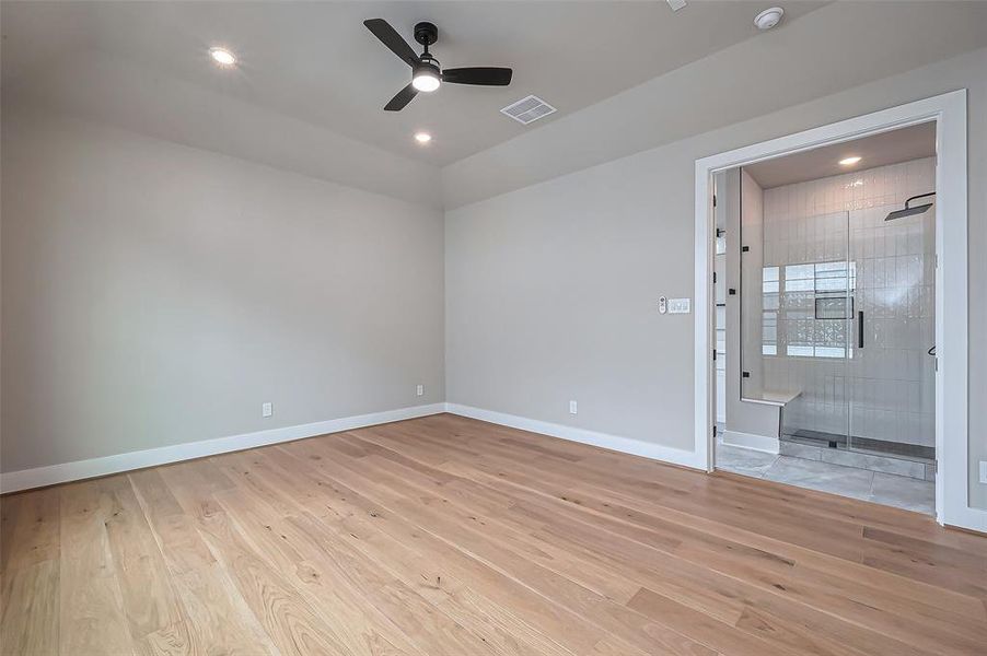 Discover a bright, spacious bedroom with elegant light wood flooring, a ceiling fan, and recessed lighting. Enjoy the convenience of an en-suite bathroom featuring a modern glass shower.