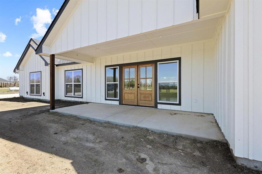 The property features a spacious covered patio with a concrete slab, board and batten siding, and dual pane windows with dark trim