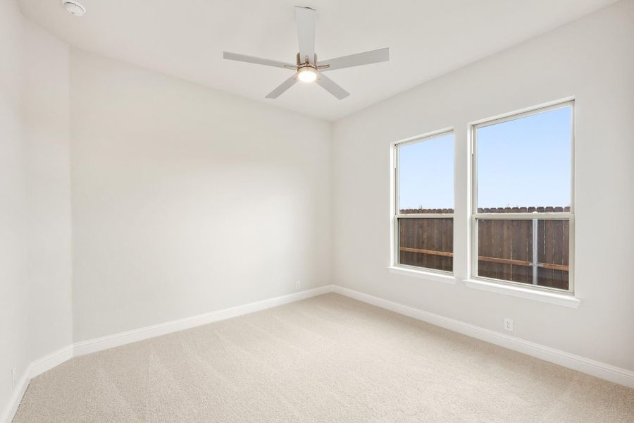 Empty bedroom with carpet flooring, ceiling fan, and two windows with backyard view