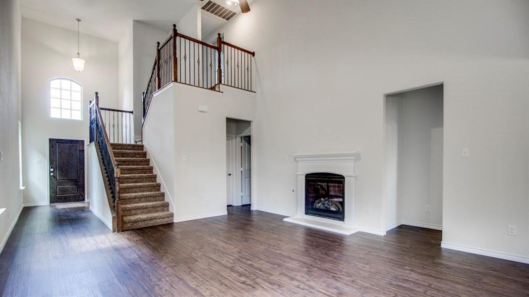 Unfurnished living room featuring a high ceiling, stairway, dark wood finished floors, and a glass covered fireplace Unfurnished living room featuring a high ceiling, stairway, dark wood finished floors, and a glass covered fireplace