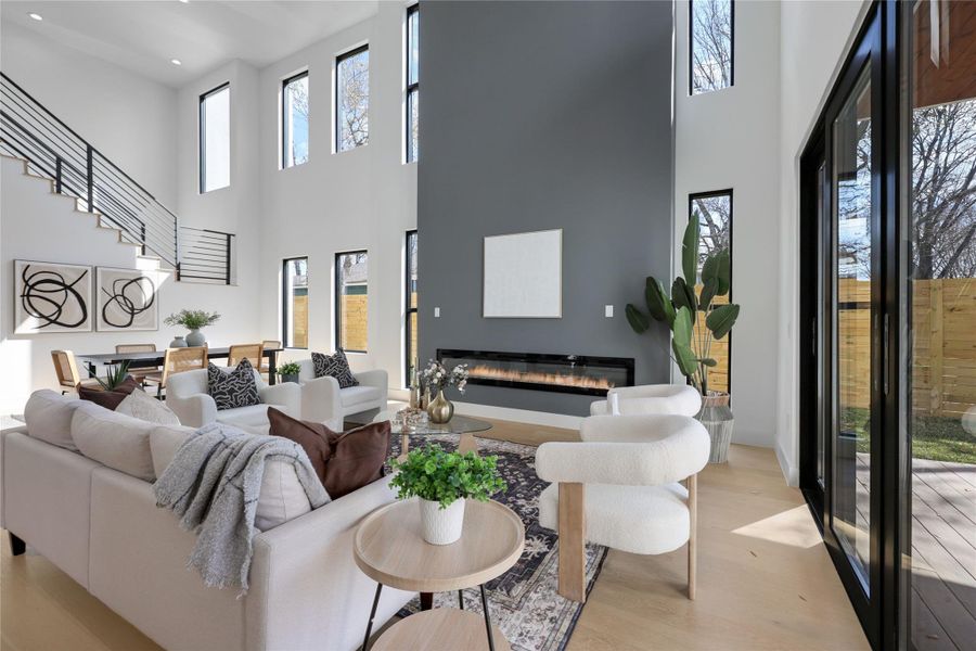 Living room with a glass covered fireplace, a high ceiling, healthy amount of natural light, and light wood-type flooring