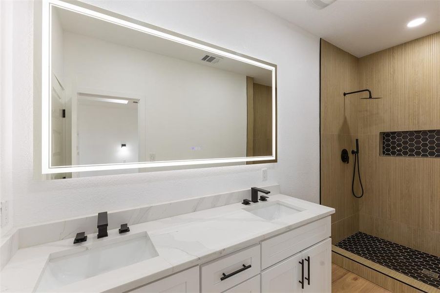 Full bathroom featuring double vanity, a tile shower, and light wood-type flooring