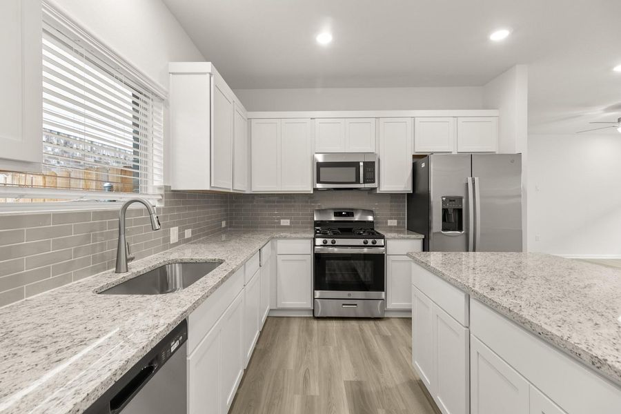 The kitchen features white cabinetry, granite countertops, and stainless steel appliances, including a refrigerator, microwave, and range