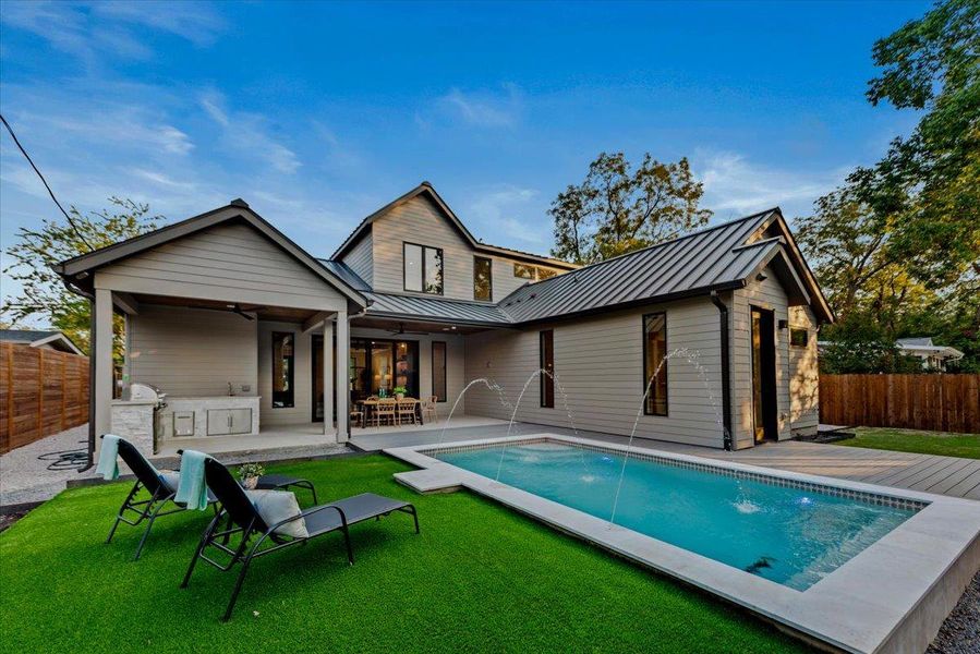 Heated, saltwater pool with turf lounge area and covered patio with outdoor kitchen.