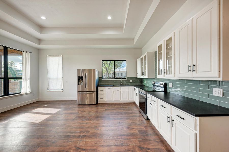 Gleaming wood floors pair with multi-tiered tray ceilings in this open modern kitchen.