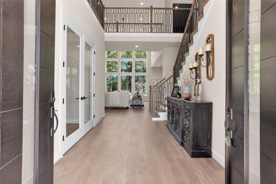 Double-door entry opens to views of the home office, elegant staircase and a wall of floor-to-ceiling windows. Warm Hickory wood floors span the entire first level, adding natural richness and flow to the open layout.