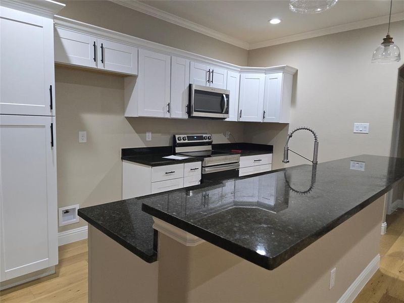 Kitchen with pendant lighting, light wood-type flooring, white cabinetry, appliances with stainless steel finishes, and ornamental molding